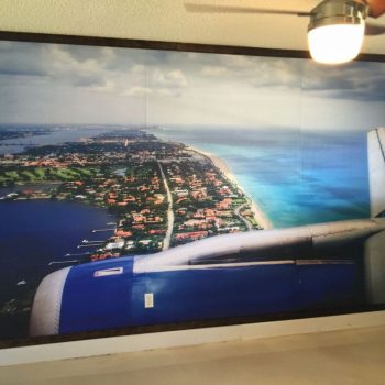Aerial view of a coastal landscape with vibrant blue ocean, green land, and airplane wing in foreground, showcasing CRD Wraps' wall wrap design.