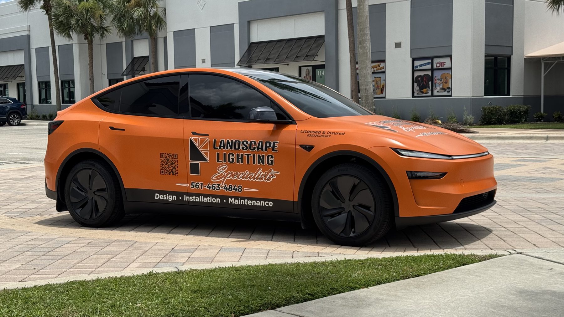 Orange Tesla Model Y commercial vehicle wrap with Landscape Lighting Specialists branding