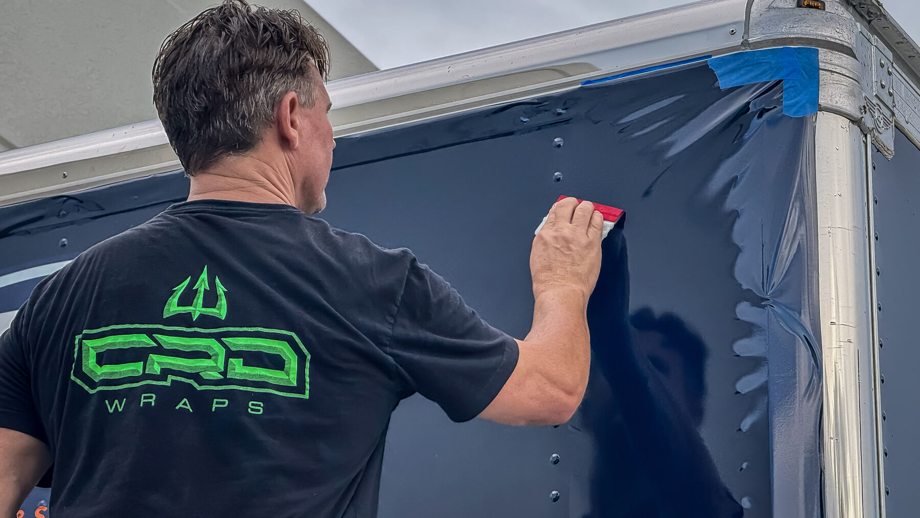 CRD Wraps installer applying dark blue printed vinyl to the riveted side of the NXT Move box truck